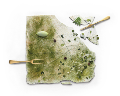 A dish of a square white substance cracking, dusted with green and garnished with small vibrant leaves