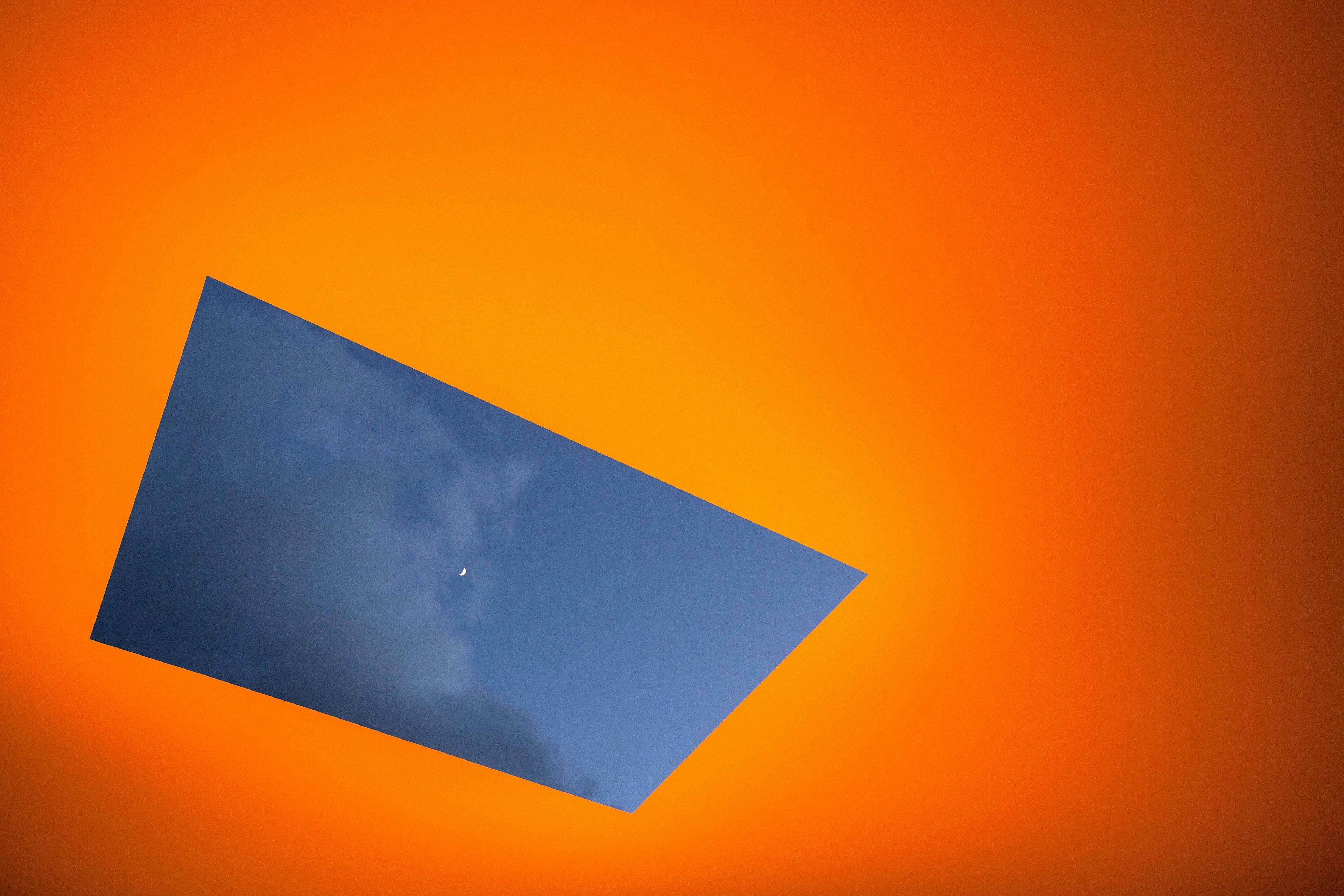 An orange lit roof with a hole showing a cloudy, dusky sky.