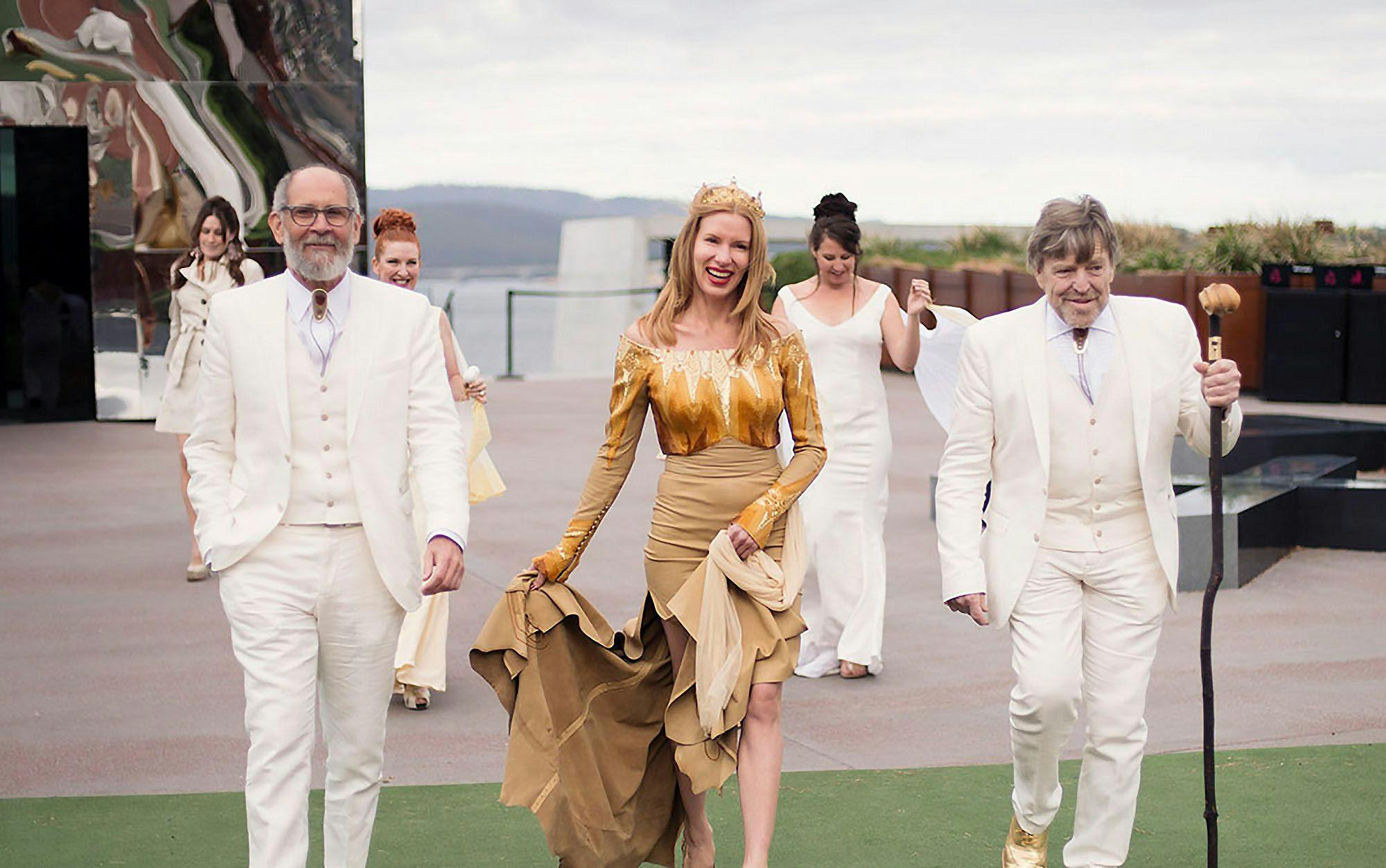 Kirsha in a gold wedding dress and crown surrounded by guests in white